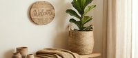 Cozy boho entryway with a woven basket holding a fiddle leaf fig plant, wooden welcome sign, knit throw, and ceramic vases on a bench.