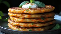 Stack of golden potato pancakes topped with sour cream and fresh mint leaves on dark plate, homemade comfort food for breakfast or dinner recipes.