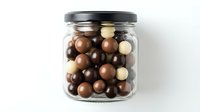 Glass jar filled with assorted chocolate balls in dark, milk and white varieties on clean background for confectionery and sweet treat designs.