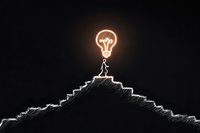 Silhouette of person standing on mountain peak with glowing light bulb above, symbolizing achievement, innovation and bright ideas against dark background.