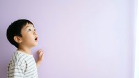Young Asian boy, approximately 3-5 years old, wearing striped shirt, looking upward with wonder and amazement against soft purple background. Suitable for childcare, education, and parenting content.