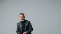 Middle-aged man with gray hair and beard wearing dark blazer and black turtleneck against neutral background. Professional portrait suitable for corporate, business, and executive use.