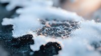 Delicate frost crystals forming intricate patterns on dark surface with soft orange glow, extreme macro photography showing natural winter ice formation.