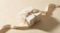 Elegant gift box wrapped in marble-textured paper with a satin beige ribbon bow on a neutral cream background with soft shadows.