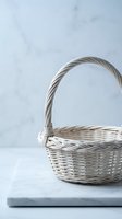 Empty wicker basket with handle on marble surface against textured wall background for home decor and storage solutions.