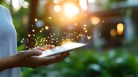Female hands holding glowing tablet device with magical sparkles and bokeh lights emerging in sunset garden atmosphere. Digital transformation concept.