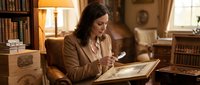 Professional businesswoman reading large book in elegant home library with warm lighting and classic furniture for educational content.