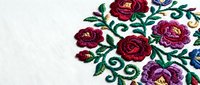 Traditional floral embroidery with red and pink roses on white fabric featuring decorative swirls and leaves for textile design and craft projects.