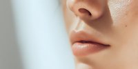 Close-up of woman's face showing natural skin texture with soft lighting highlighting nose and lips for skincare and beauty concepts.