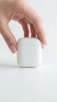 Woman's hand holding a white wireless earbuds charging case on a light background, showcasing modern audio technology.
