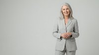 Professional mature businesswoman with silver hair in gray suit smiling confidently against neutral background for corporate presentations.