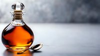 Amber liquid in glass decanter with stopper and spoon on neutral surface, suitable for beverage, alcohol, and culinary content.