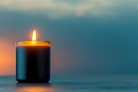 Glowing black scented candle with warm flame against blurred teal background creates peaceful ambiance for spa, meditation, or home decor setting.