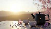 Peaceful tea ceremony setup with black teapot and cup on wooden table during golden hour sunset with cherry blossoms and scattered petals creating serene atmosphere.