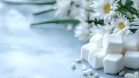 Fresh white marshmallows arranged with delicate daisies on light blue surface, creating soft dreamy composition for food photography and lifestyle blogs.