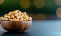 Roasted peanuts in wooden bowl on dark surface with warm bokeh lights background for healthy snacking and cooking ingredients.