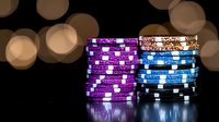 Stacked casino poker chips in purple, blue and black with white spots on dark background with bokeh lights, reflecting on glossy surface. For gambling concepts.