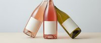 Three wine bottles with blank labels in rose, red and white varieties arranged on wooden surface for branding mockup and product presentation.
