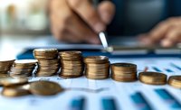 Stacks of gold coins on financial documents with person analyzing data in background, representing business growth and investment planning concept.