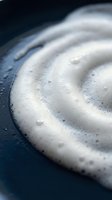 Creamy white foam swirl with bubbles on dark surface for skincare cosmetics beauty products and spa treatments.