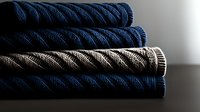 Folded navy blue and gray textured bath towels stacked on dark surface with dramatic side lighting creating contrast between light and shadows.