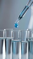 Laboratory pipette dropping blue liquid into test tubes for scientific research and chemical analysis experiments.