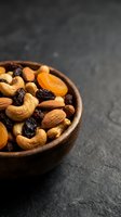Mixed nuts and dried fruits in wooden bowl on dark stone surface for healthy snacking and cooking ingredients.