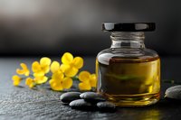 Aromatherapy essential oil in glass bottle with yellow flowers and zen stones on dark slate background, spa wellness concept for natural cosmetics.