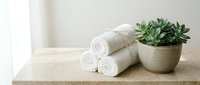 Clean white towels stacked on wooden surface with green succulent plant in woven basket for spa wellness bathroom decor and home organization.