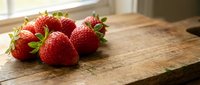 Fresh ripe strawberries on rustic wooden cutting board in bright kitchen setting for healthy cooking and food preparation concepts.