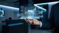 Businessman in dark suit holding glowing digital holographic display with financial charts, graphs, and data analytics icons floating above palm in modern office environment.