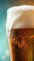 Chilled lager beer with thick foam head and condensation droplets in glass against turquoise background, suitable for beverage advertising and hospitality marketing.
