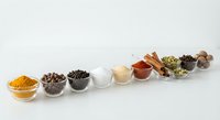 Colorful spices and seasonings arranged in glass bowls on white background for culinary cooking and food preparation projects.