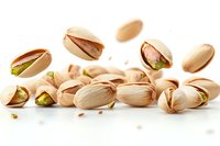 Fresh roasted pistachios scattered and falling on white surface, macro shot showing detailed texture of nuts, shells and green kernels in natural light.