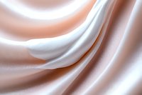Smooth flowing waves of white and peach colored silk fabric create elegant abstract curves and folds with soft lighting effects. Luxury background design.