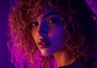Young mixed race woman with curly hair in neon purple and red lighting, dramatic portrait with moody atmosphere and glowing skin highlighting facial features.