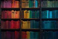 Colorful rainbow bookshelf with vintage books arranged by color from red to blue in wooden shelving, creating vibrant spectrum display.