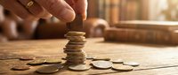 Male hand stacking gold coins on wooden surface with blurred background, representing financial growth, savings, investment, and wealth accumulation for business concepts.