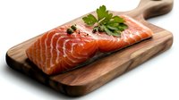 Fresh raw salmon fillet with parsley garnish on wooden cutting board against white background, ready for cooking preparation. Healthy seafood concept.