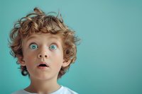 Young boy with curly blonde hair and bright blue eyes expressing surprise and wonder against turquoise background, wearing white t-shirt. Emotional portrait captures childhood amazement.