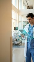 Young male doctor in blue scrubs examining digital tablet with medical data in modern hospital corridor with natural lighting and medical equipment.