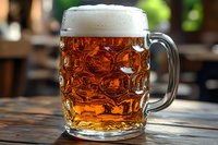 Traditional glass beer mug with fresh cold amber lager and white foam head on rustic wooden table, selective focus with blurred background.