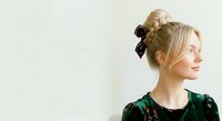 Young woman with blonde hair styled in an updo with black velvet bow, wearing dark green velvet top, looking to the side against white background for fashion and beauty content.