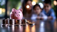 Pink ceramic piggy bank with stacked coins on wooden table against blurred background with bokeh lights, representing savings and financial planning.