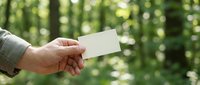 Hand holding blank white business card outdoors with green bokeh background for mockup and branding design projects.