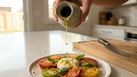 Close-up of olive oil being drizzled over roasted vegetables and fresh greens on a white plate in a modern kitchen, perfect for food blogs, recipes, and culinary content.