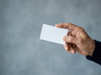 Male hand holding blank white business card against blurred gray background, suitable for corporate branding, marketing mockups, and professional identity design.