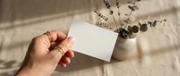 Female hand holding blank white business card mockup with dried eucalyptus branches and lavender in soft natural lighting for branding design.