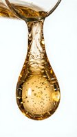 Golden oil pouring into teardrop shape with bubbles, isolated on white background for culinary, cosmetic, and wellness design projects.