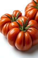 Fresh ripe red heirloom tomatoes with green stems on white background, macro close-up view showing natural texture and ribbed surface detail.